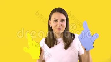 一个穿着白色T恤的女人正在黄色背景上跳舞，里拿着蓝色和黄色的卡通手。 乐趣